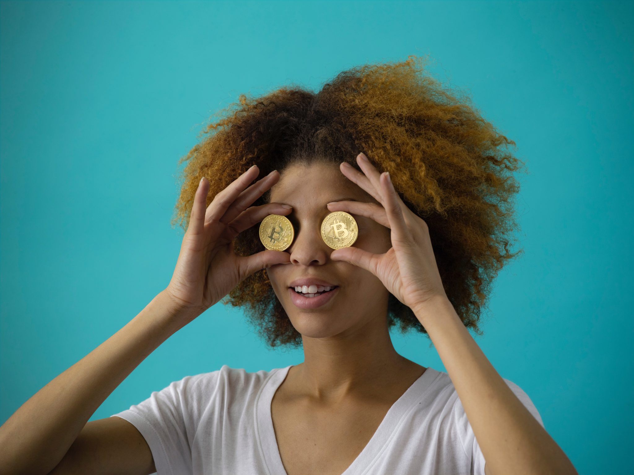  A freelancer holding Bitcoin coins over her eyes, symbolizing the search for competitive rates.